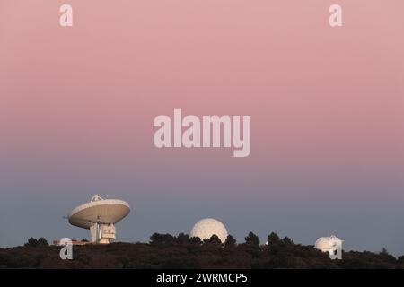 Satellite and scientific observatory stations with large dishes against a serene pastel-colored sunset sky Stock Photo