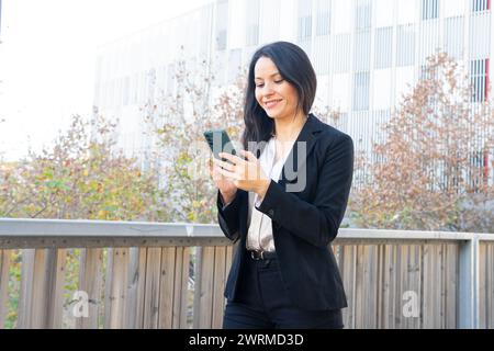 A professional woman in a business suit using her smartphone, standing outside an office building. Stock Photo