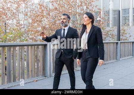 Two professional business colleagues, a man and a woman, engaged in a discussion while walking together outside an office building. Stock Photo