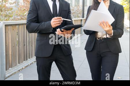 Cropped unrecognizable man and woman business colleagues in formal attire discussing work and analyzing documents on a tablet outside. Stock Photo