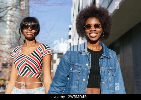 Two stylish African American sisters radiate happiness as they stroll through the city, enjoying the warm sunlight together Stock Photo