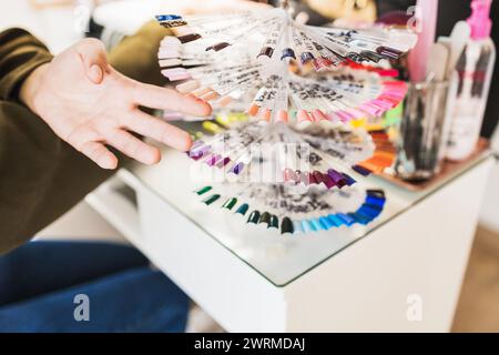 A person's hand is selecting from a variety of nail polish color samples displayed in a fan arrangement at a salon Stock Photo