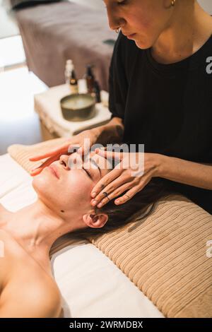 A therapist giving a relaxing facial massage to a female client in a serene spa setting Stock Photo