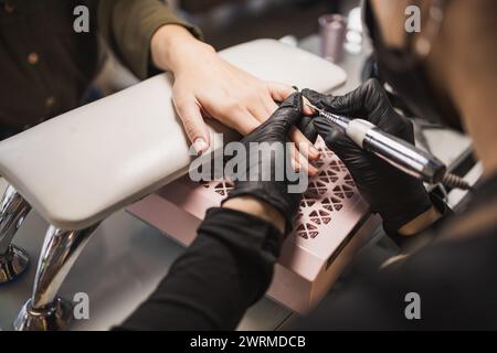 Close-up shot of a nail technician's hands using a drill machine for a manicure on a client's nails in a salon Stock Photo