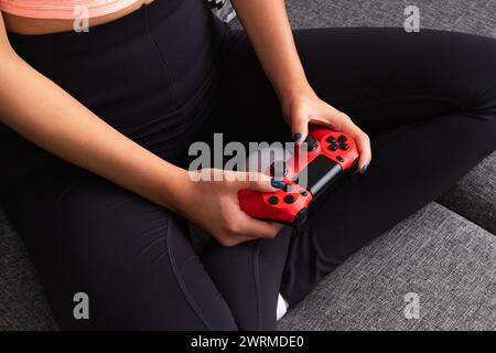 From above cropped unrecognizable woman sitting comfortably with a red game controller in her hands Stock Photo