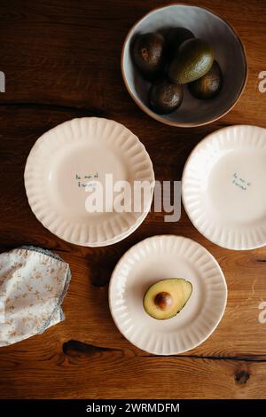 An artistic top-down view of ripe avocados in a bowl and halved on plates with handwritten phrases on a wooden surface Stock Photo