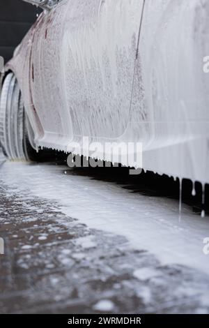 Close-up of a car covered in soapy foam, with focus on the dripping suds, during a car wash service Stock Photo