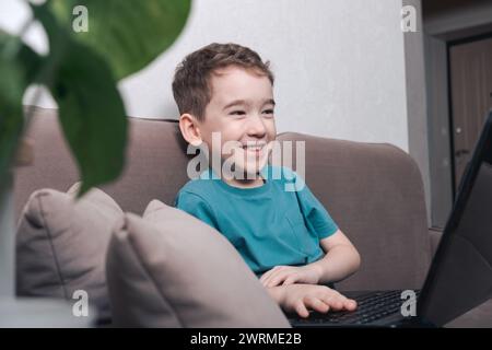 Smiling child using a laptop at home, depicting modern kids' interaction with technology. Stock Photo