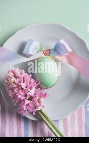 Top view soft pastel-hued Easter setting featuring a decorated egg tied with a multi-colored ribbon on a white plate, accompanied by pink hyacinth flo Stock Photo