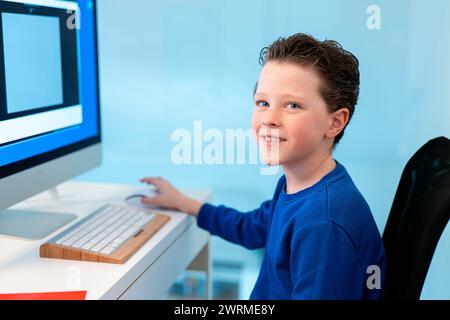 A smiling boy enjoys his time on the computer, possibly participating in a virtual class or exploring educational software Stock Photo