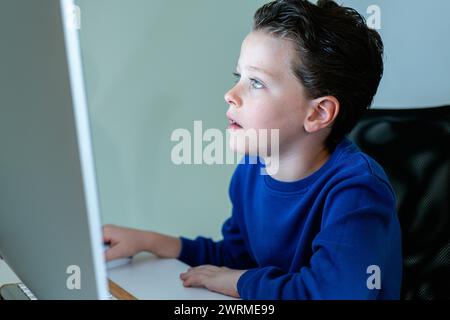 A young boy with a look of concentration while using a computer in a home environment, potentially engaged in online learning Stock Photo