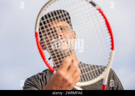An unrecognizable man holds a tennis racket in front of his face, partially obscuring his features. Stock Photo