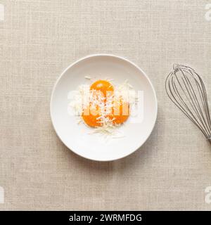 From above two raw egg yolks nestled in grated cheese with a whisk on the side, ready for making Spaghetti Carbonara. Stock Photo