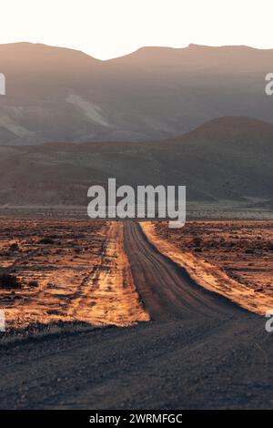 The setting sun casts a warm glow over a winding dirt road through the Patagonian desert, inviting adventure in the tranquil evening Stock Photo