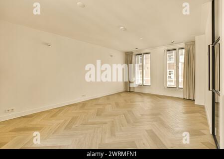 An empty living room with sunlight flooding through three large windows, reflecting off herringbone-patterned wooden floors and plain white walls. Stock Photo