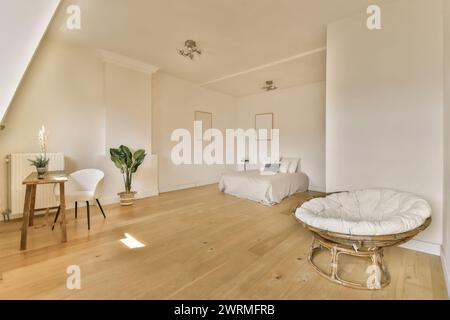 Minimalist attic bedroom with hardwood flooring, a cozy bed, white walls, and modern furniture basking in natural light. Stock Photo