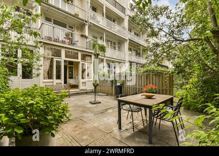 A tranquil patio area featuring outdoor furniture and lush greenery beneath a white apartment building with balconies. Stock Photo