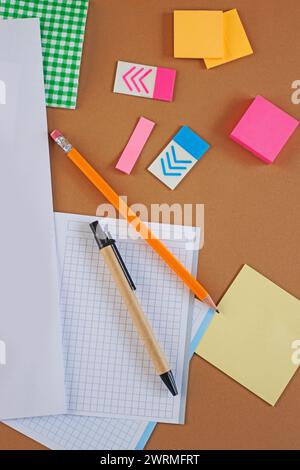 Overhead view of office supplies including sticky notes, graph paper, and pencils on a brown surface, creating a neat and organized workspace concept. Stock Photo