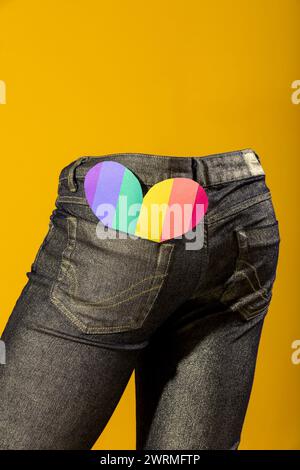 A vibrant heart cutout peeks from the back pocket of a denim jean against a solid yellow backdrop, symbolizing love and happiness Stock Photo