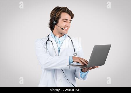 Smiling man doctor with headset using laptop for telehealth services Stock Photo