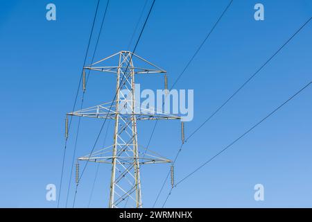 Overhead 132kv electricity transmission cables and transmission tower against a blue sky. Stock Photo