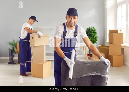 Movers male professional team in overalls loading, packing and unloading items with care, wrapping Stock Photo