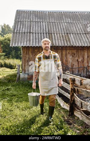 good looking bearded man with tattoos on arms holding bucket with fresh milk while on his farm Stock Photo