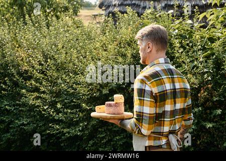 good looking man with tattoos on arms in casual attire holding cheese and looking away while on farm Stock Photo