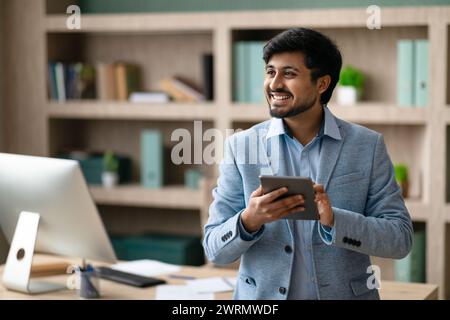 Happy Indian programmer man using tablet standing in modern office Stock Photo