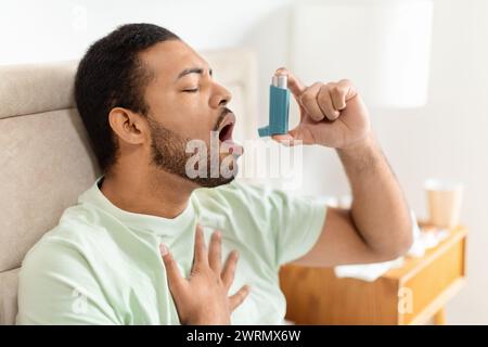 Handsome black man sitting alone at home, using asthma pump Stock Photo