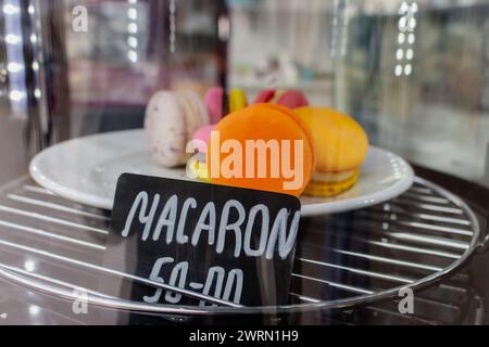 Macaroons on showcase in cafe. Macaron cake with price tag. Sweet food concept. Morning dessert. Orange macaron on plate in marketplace. Stock Photo