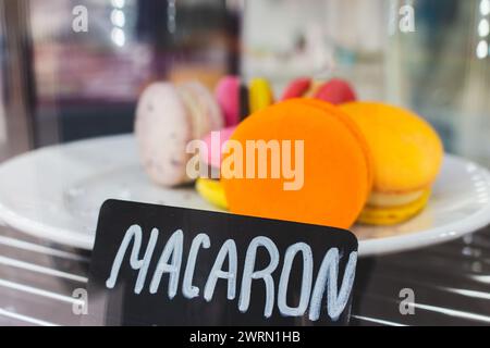 Macaroons on showcase in cafe. Macaron cake with price tag. Sweet food concept. Morning dessert. Orange macaron on plate in marketplace. Stock Photo