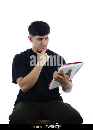 Concentrated young man looks at his notebook, seated with white background. Analysis, entrepreneurship and financial education Stock Photo