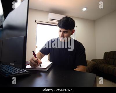 Image of a college student doing homework at home, sitting in front of his computer. Distance education, academic work and online learning Stock Photo