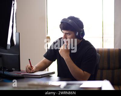 Image of a concentrated young man participating in a live broadcast taking notes in a notebook Stock Photo