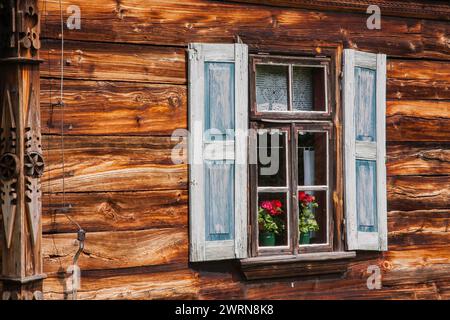 A window of an old country house with wooden shutters and flowers behind the glass Stock Photo