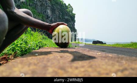 View of an African man with a machete cutting a coconut, with Santa Catarina tunnel as a background in Sao Tome, Africa Stock Photo