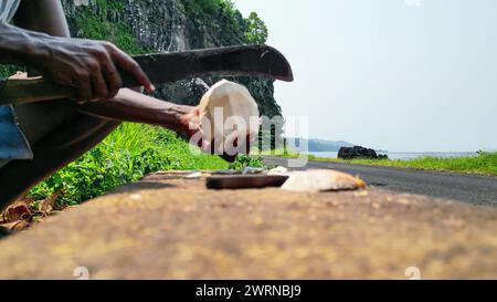 View of an African man with a machete cutting a coconut, with Santa Catarina tunnel as a background in Sao Tome, Africa Stock Photo