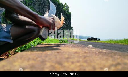 View of an African man cutting a coconut, with the Santa Catarina tunnel as background at Sao Tome,Africa Stock Photo