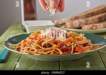 Turkey mince bolognese with cheese being sprinkled over it and some bread in the background. Stock Photo