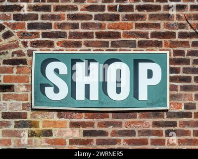 A wooden sign mounted on a brick wall with the word 'shop' hand-painted on it. Stock Photo