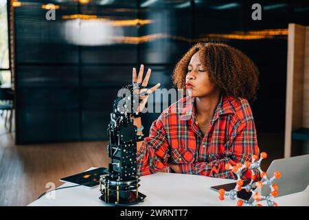 In a classroom a smart teenager experiments with a humanoid robotic hand showcasing joy in learning Stock Photo