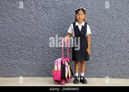 4 year old Latina brunette girl with eyeglasses, uniform and backpack walks to school this back to school Stock Photo