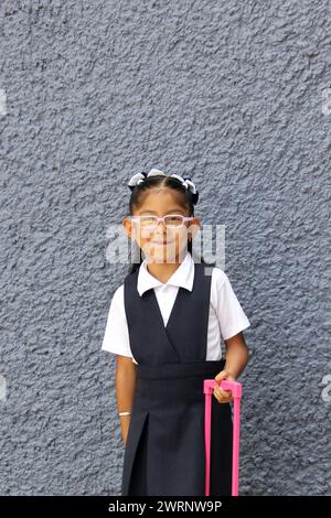 4 year old Latina brunette girl with eyeglasses, uniform and backpack walks to school this back to school Stock Photo