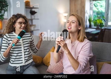Two female friends having fun singing with hairbrushes as microphones at home Stock Photo