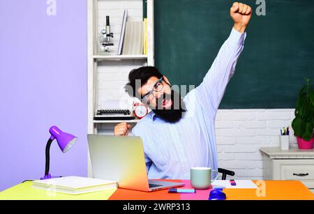 Happy male teacher or student in classroom. Bearded businessman professional coach, teacher or university professor sitting at desk in office Stock Photo