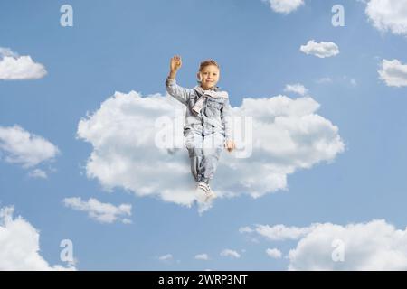 Child in jeans sitting on a cloud and waving Stock Photo