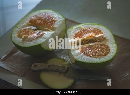 A halved Pomelo, ready to be eaten, sits on a wooden cutting board. Stock Photo