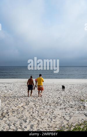People walking towards the Atlantic Ocean waters on the empty Praia Seca beach close to Sao Judas Tadeu street under summer afternoon clouded sky. Stock Photo