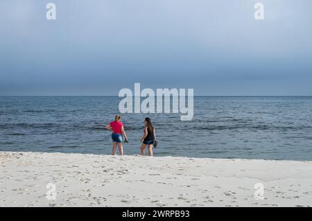 Two woman standing on the empty Praia Seca beach at Atlantic Ocean blue waters close to Sao Judas Tadeu street under summer afternoon clouded sky. Stock Photo